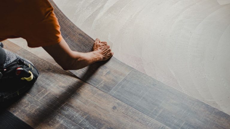 Construction worker installing new vinyl tile floor using glue down method